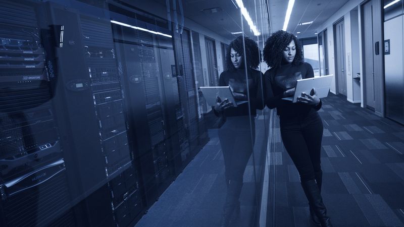 Two engineers working from tablets in a data centre corridor.