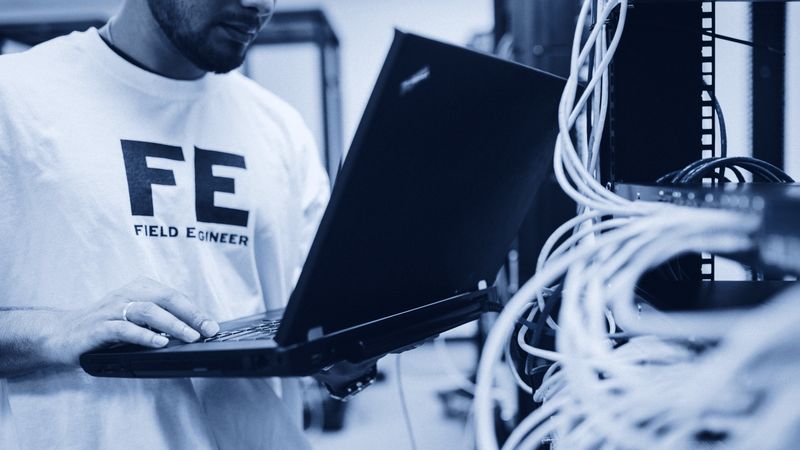 A field engineer working from a laptop at a network cabinet.